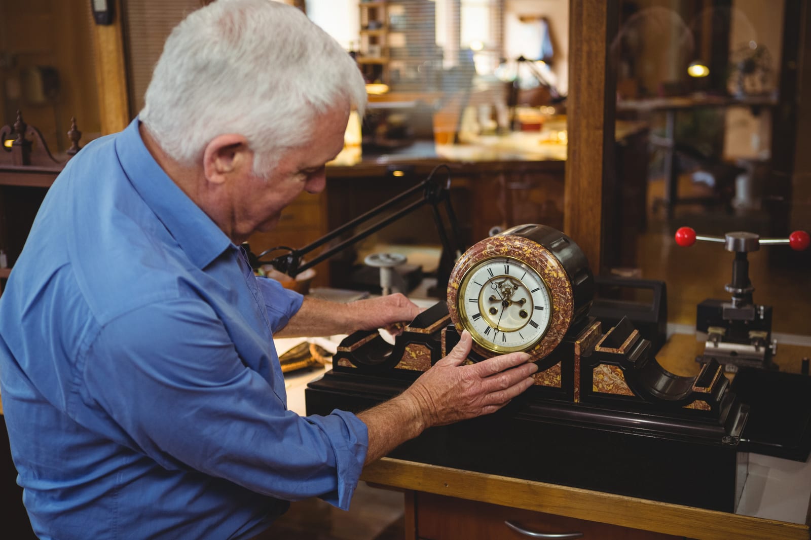 Orologiaio regola un orologio da tavolo antico al banco di lavoro